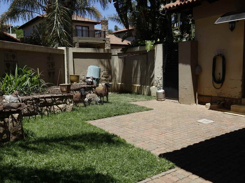A rear garden area featuring a paved patio, lawn, and stone retaining wall, enclosed by a boundary wall showing signs of weathered paint and plaster.