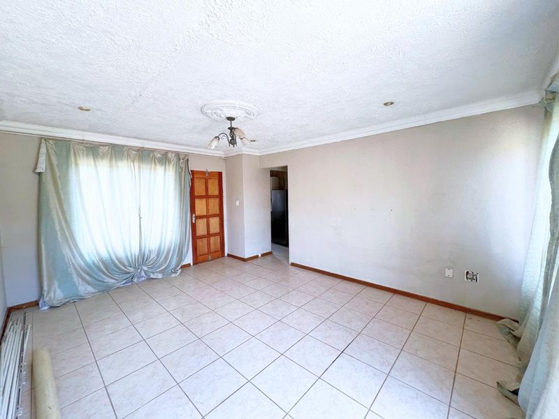 An empty living room featuring tiled flooring, decorative ceiling rose, and coving, providing a blank canvas for interior design updates.