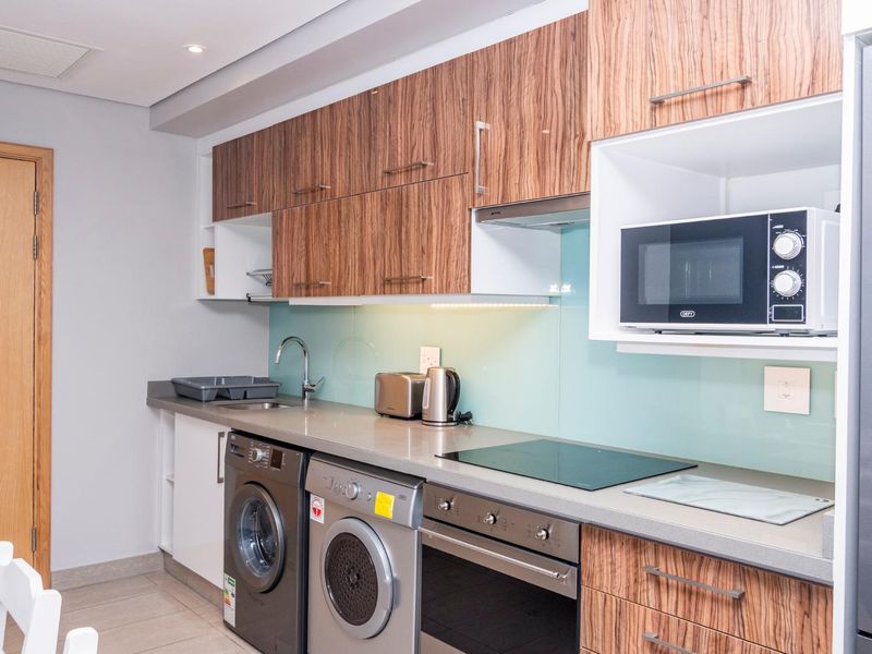 Modern kitchen featuring wood-grain cabinetry, stone countertops, glass splashback, integrated appliances, and built-in laundry facilities.