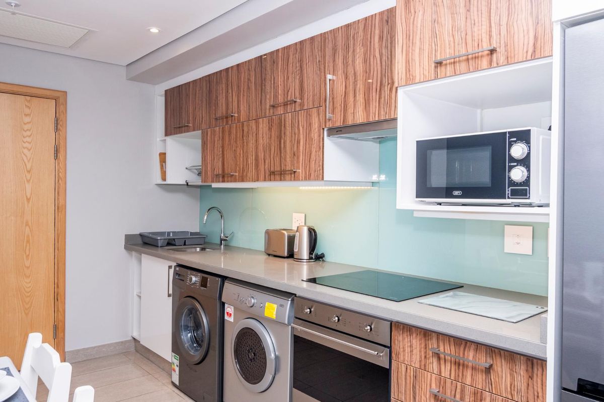Modern kitchen featuring wood-grain cabinetry, stone countertops, glass splashback, integrated appliances, and built-in laundry facilities.