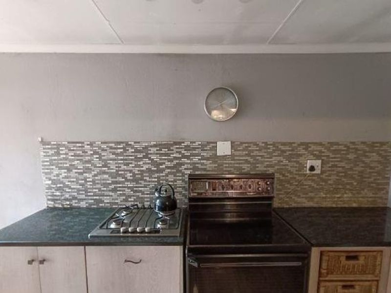A kitchen area featuring a gas hob, freestanding oven, mosaic tile backsplash, and laminate countertops with built-in cabinetry.