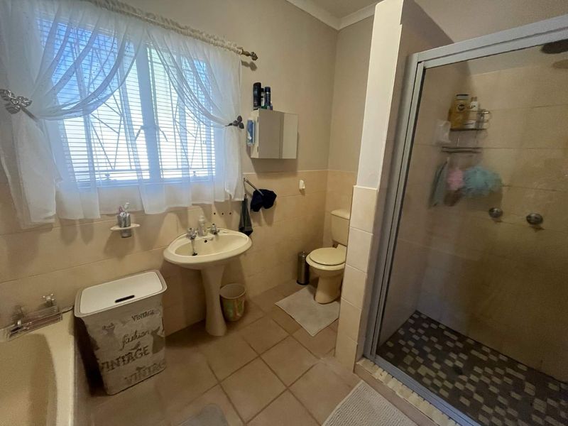Functional bathroom featuring a pedestal basin, shower enclosure, and tiled finishes, offering a practical layout with potential for modern updates.