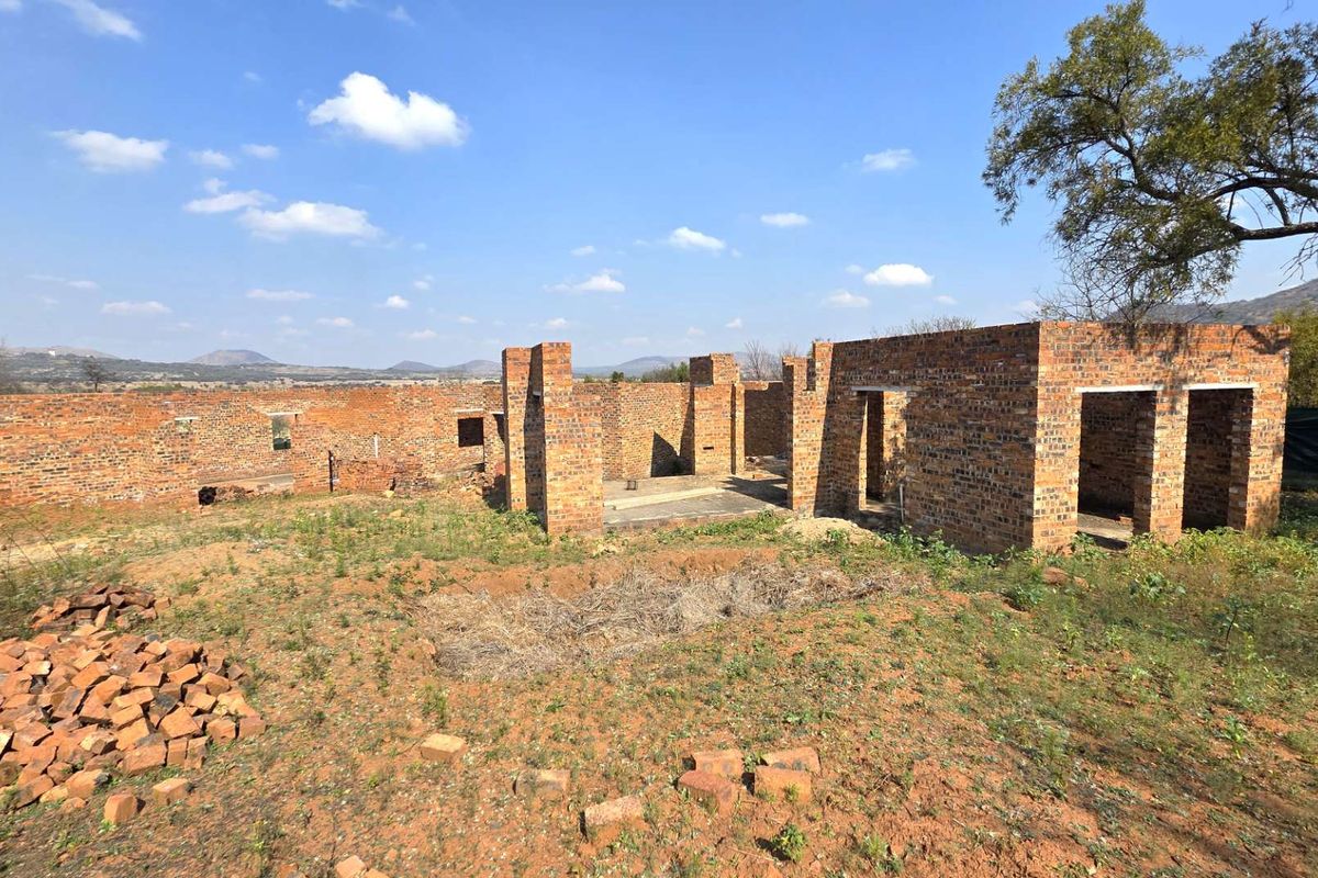 An exterior view of a residential property currently under construction, featuring exposed brick walls and a foundation on a large plot of land.