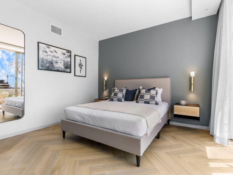 Modern bedroom featuring herringbone timber flooring, a feature wall, wall-mounted lighting, and direct access to a private balcony.