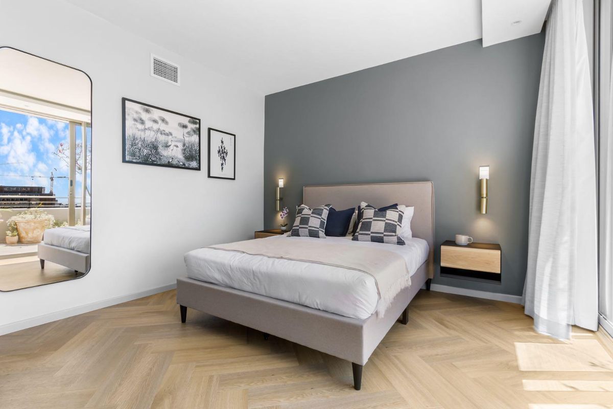 Modern bedroom featuring herringbone timber flooring, a feature wall, wall-mounted lighting, and direct access to a private balcony.