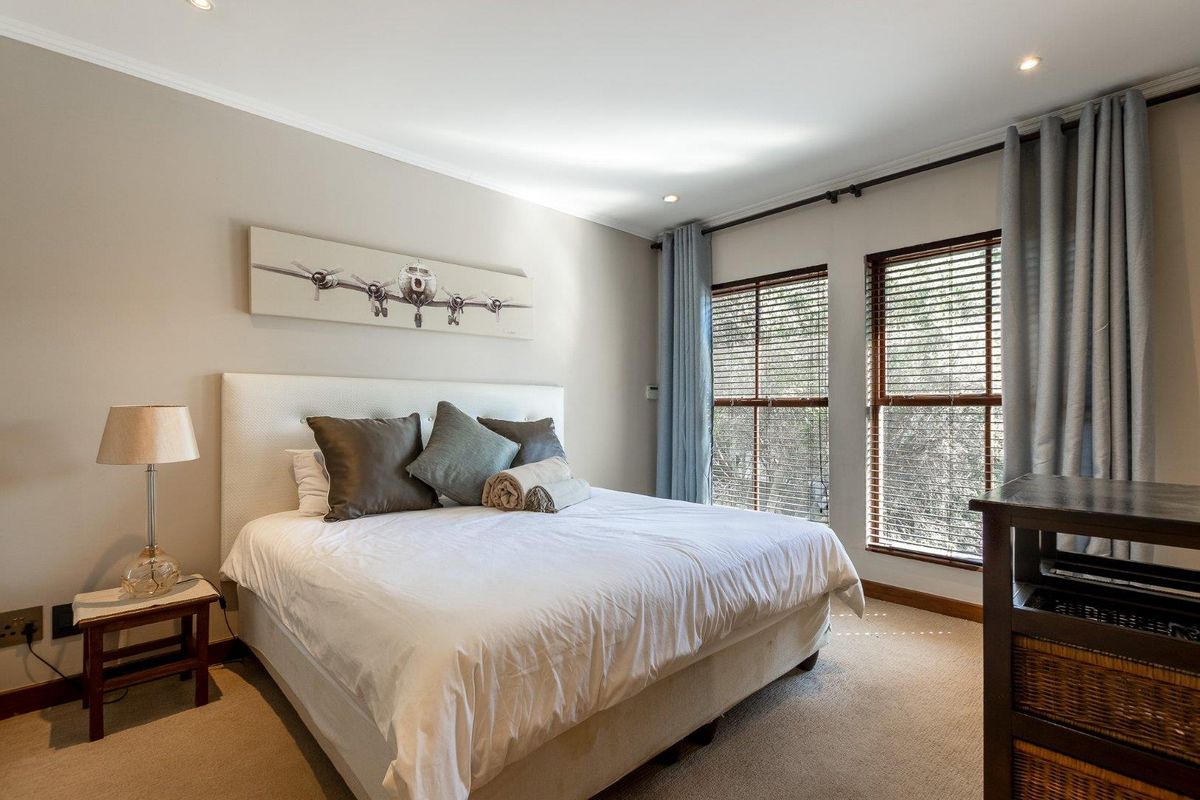 A well-maintained bedroom featuring neutral wall tones, carpet flooring, recessed downlights, and large windows fitted with venetian blinds.