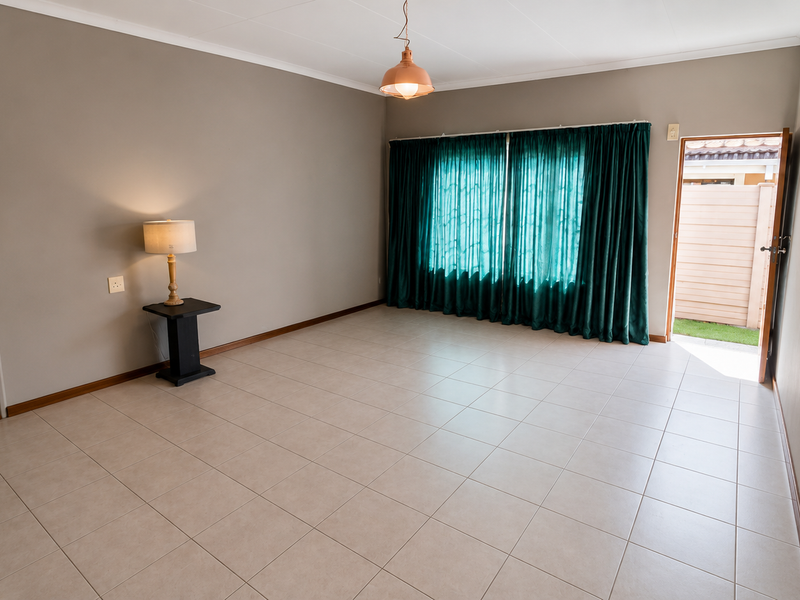 A spacious, empty living room featuring neutral tiled flooring, a pendant light fixture, and direct access to an outdoor area through a side door.