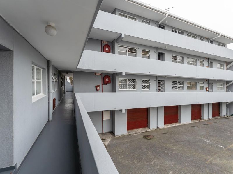 Exterior view of an apartment complex featuring concrete walkways, security bars on windows, fire safety equipment, and ground-level garage access.