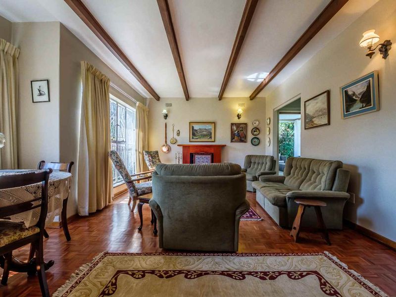 A traditional living room featuring warm parquet flooring, exposed timber ceiling beams, and a central fireplace, creating a cozy and classic atmosphere.