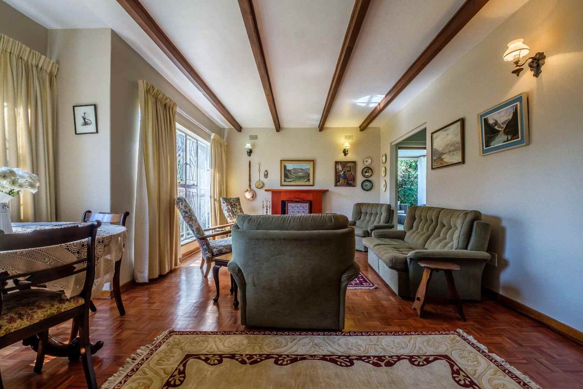 A traditional living room featuring warm parquet flooring, exposed timber ceiling beams, and a central fireplace, creating a cozy and classic atmosphere.