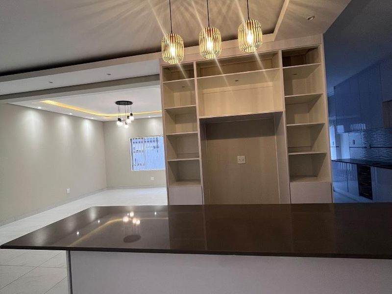 Modern open-plan living area featuring a kitchen island with stone countertop, built-in shelving, and contemporary pendant lighting throughout the spacious interior.
