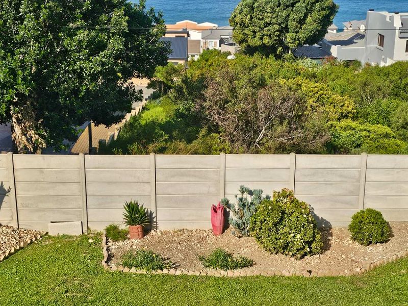 A rear garden view featuring a well-maintained lawn, landscaped garden beds, and a secure precast concrete boundary wall.