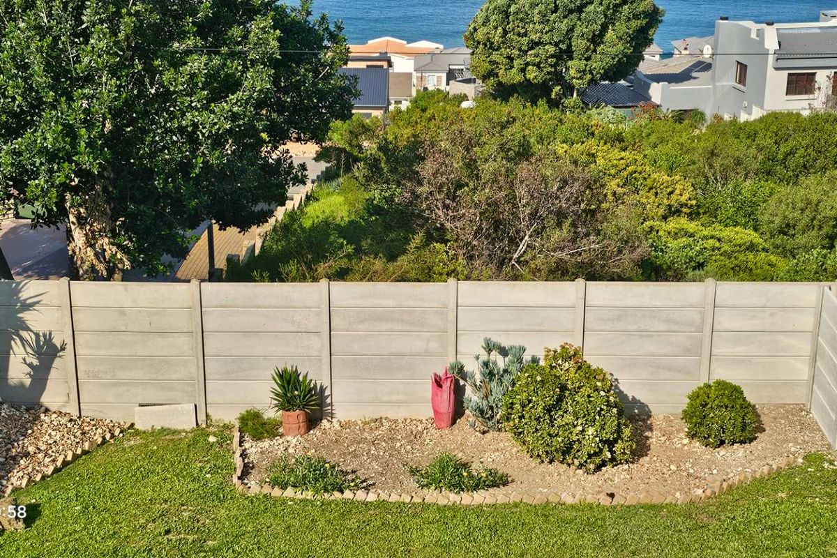 A rear garden view featuring a well-maintained lawn, landscaped garden beds, and a secure precast concrete boundary wall.