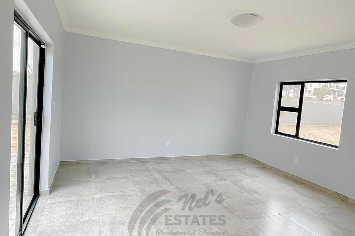 A bright, empty living room featuring neutral tiled flooring, modern black-framed windows, and a sliding glass door leading to the exterior.