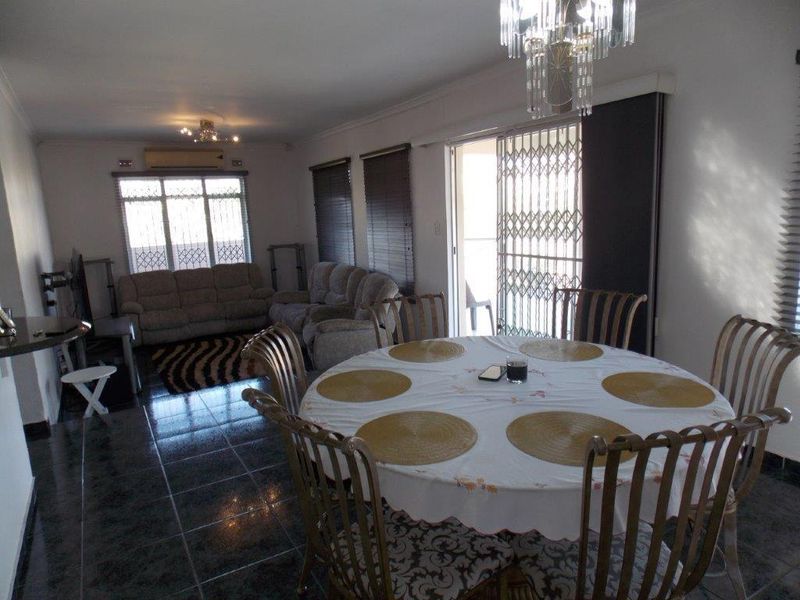 Open-plan living and dining area featuring dark tiled flooring, a crystal chandelier, and direct access to an outdoor space via a sliding security door.