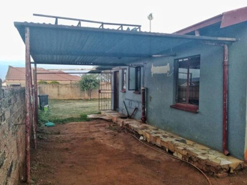 Rear exterior view of the property featuring a covered patio area with metal roofing, stone-clad base, and a surrounding boundary wall.