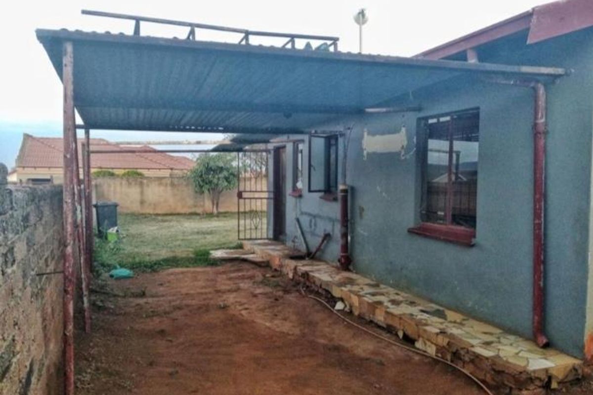 Rear exterior view of the property featuring a covered patio area with metal roofing, stone-clad base, and a surrounding boundary wall.