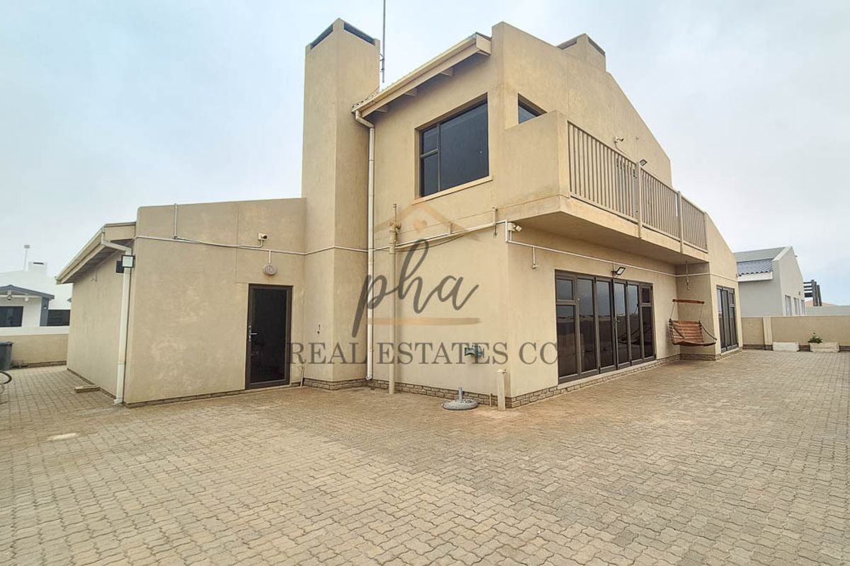 Rear view of a two-story house featuring a paved courtyard, balcony, and large sliding glass doors.