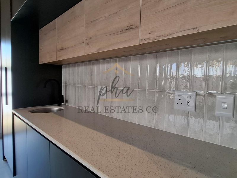 Modern kitchen area featuring sleek dark cabinetry, light wood-tone upper cabinets, stone countertops, and a stylish subway tile backsplash.