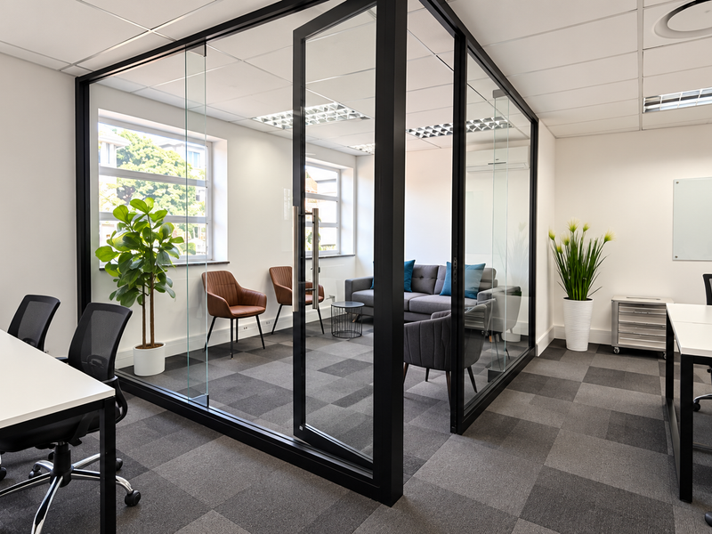 Modern office space featuring a glass-partitioned meeting room, suspended ceiling with recessed lighting, and professional carpet tile flooring.