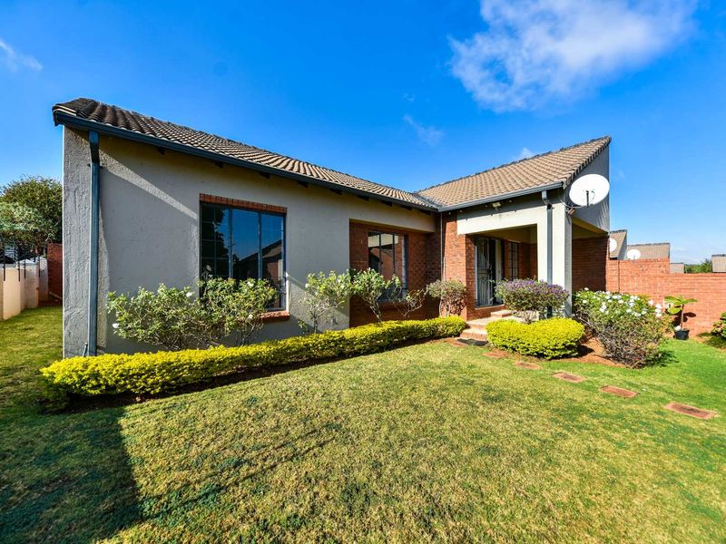 Rear view of the townhouse featuring a tiled roof, brick and plastered exterior walls, and a well-maintained garden with a paved walkway.