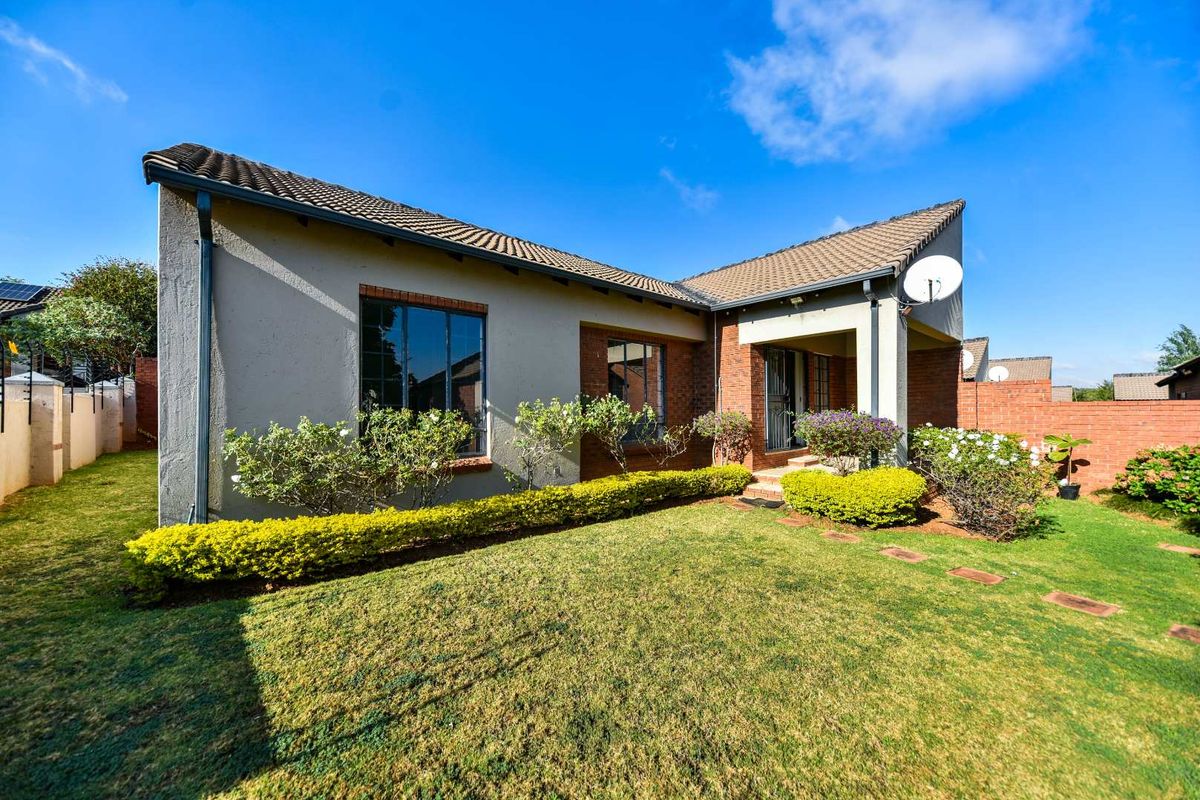 Rear view of the townhouse featuring a tiled roof, brick and plastered exterior walls, and a well-maintained garden with a paved walkway.