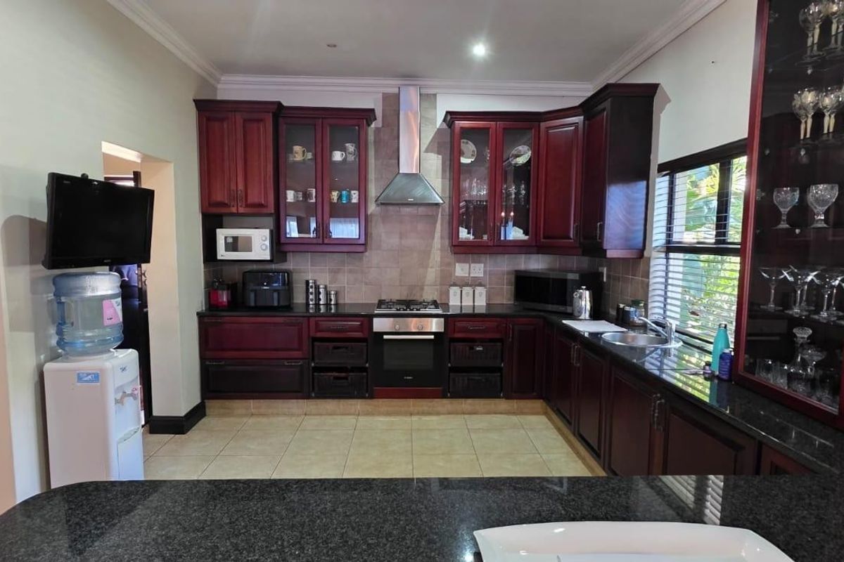 A well-appointed kitchen featuring dark wood cabinetry, granite countertops, a stainless steel extractor fan, and integrated appliances with ample storage space.