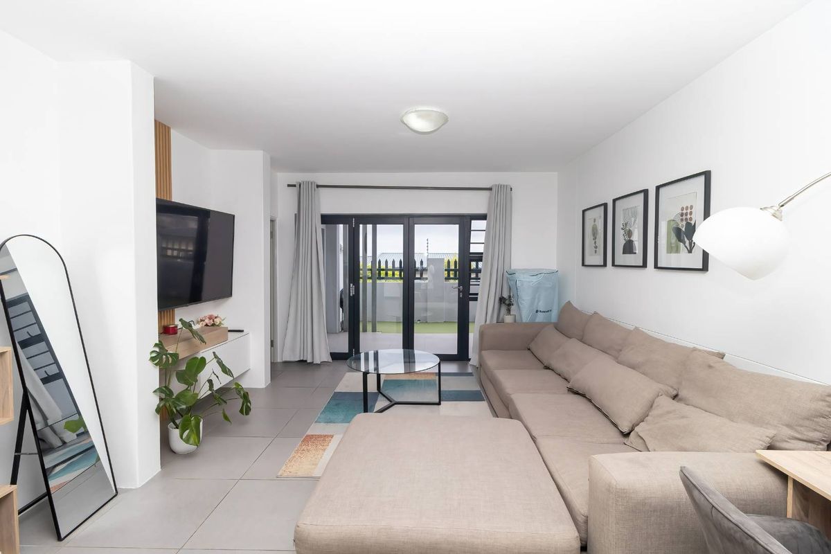 A bright and modern living room featuring large format floor tiles and sliding glass doors that provide direct access to an outdoor patio area.