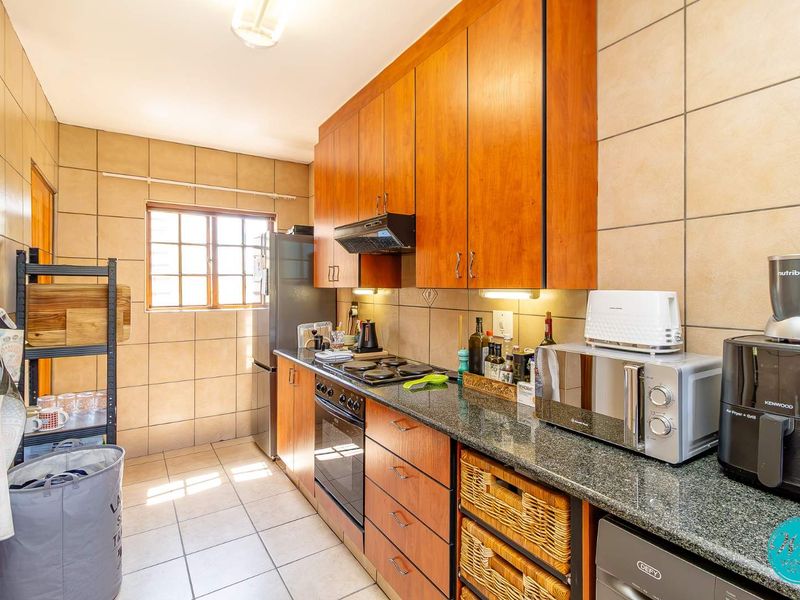A functional kitchen featuring wood-finish cabinetry, granite countertops, a built-in oven with hob, and tiled wall finishes.