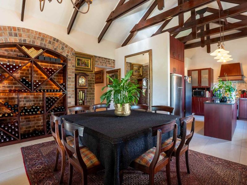 Spacious open-plan dining and kitchen area featuring vaulted ceilings with exposed timber beams, a custom brick wine rack, and modern fitted cabinetry.