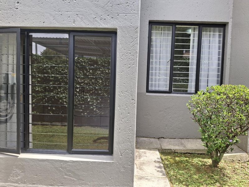Rear exterior view of the apartment featuring textured walls, security bars on windows, and a paved walkway leading along the building.