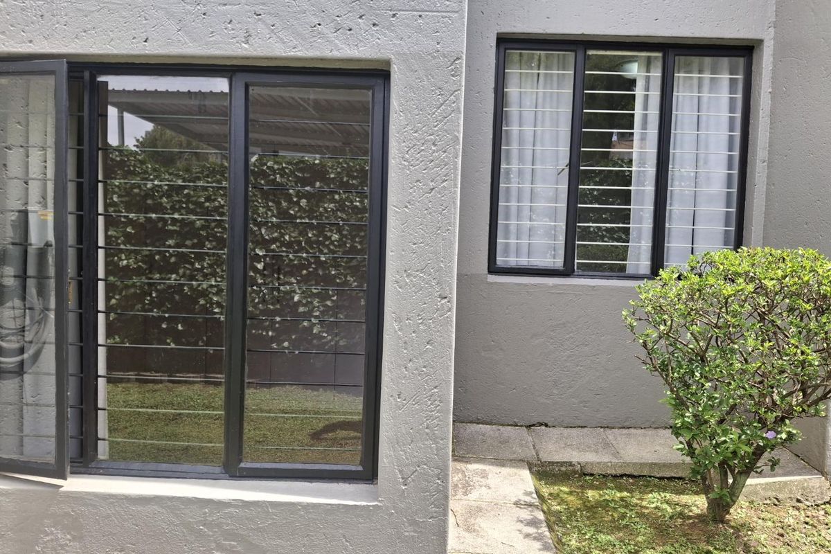 Rear exterior view of the apartment featuring textured walls, security bars on windows, and a paved walkway leading along the building.