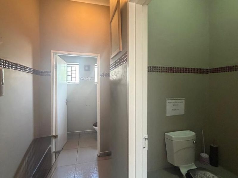 A functional office restroom facility featuring tiled flooring, decorative wall accents, and a standard flush toilet.