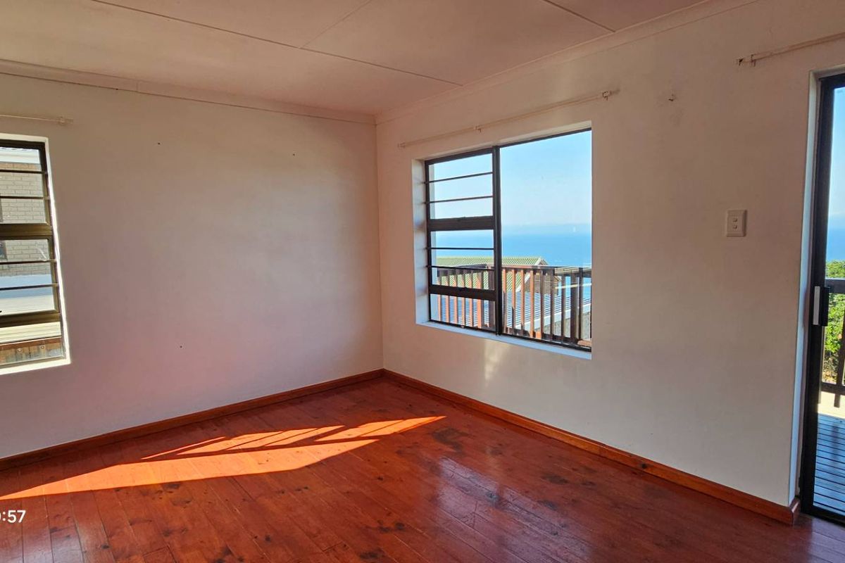 Bright and spacious bedroom featuring polished timber flooring, large windows with ocean views, and direct access to an outdoor balcony.
