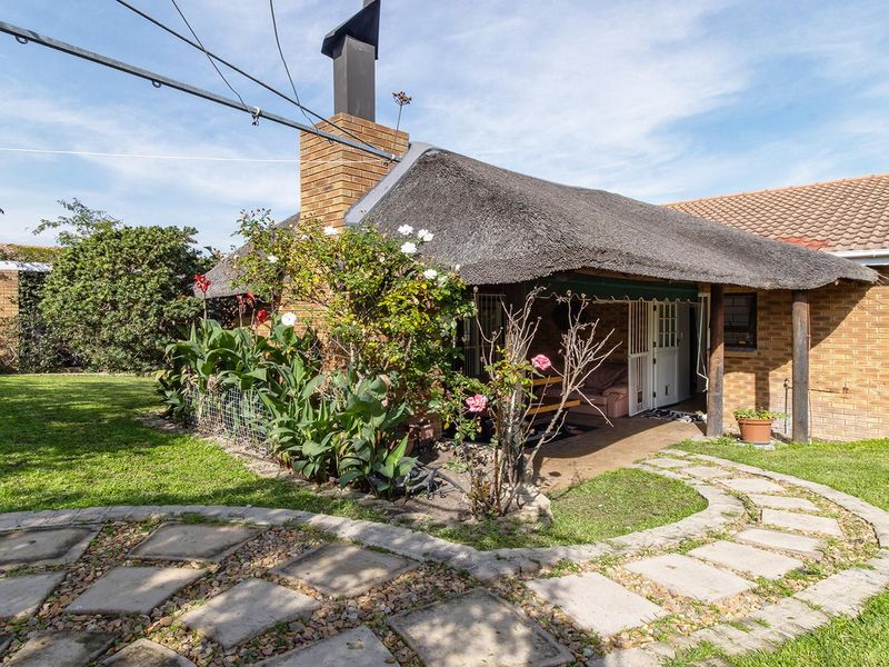 Rear view of the property featuring a covered patio with a thatch roof, brick chimney, and a paved garden walkway.