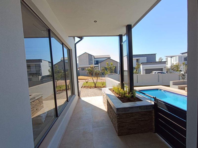 A modern covered patio featuring tiled flooring, a built-in stone-clad planter, and direct access to a private swimming pool.