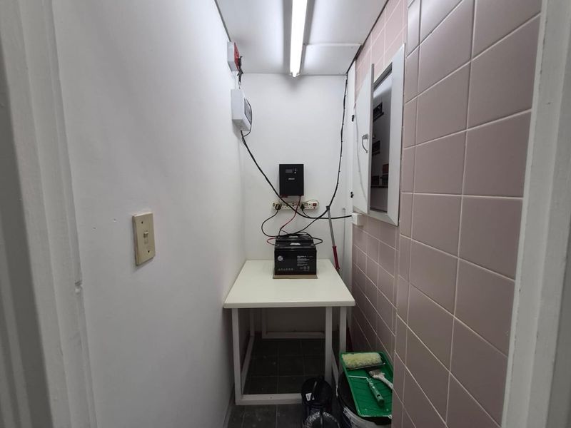 A compact utility space featuring an electrical distribution board, tiled wall finishes, and an installed power inverter system.
