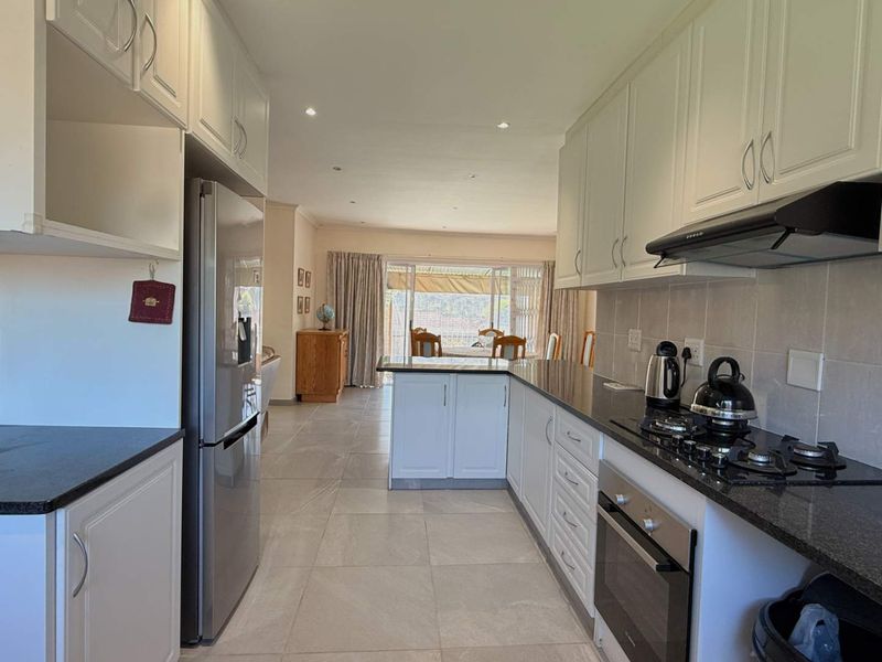 Open-plan kitchen featuring white cabinetry, granite countertops, gas hob, and integrated appliances, flowing seamlessly into the dining and living area.