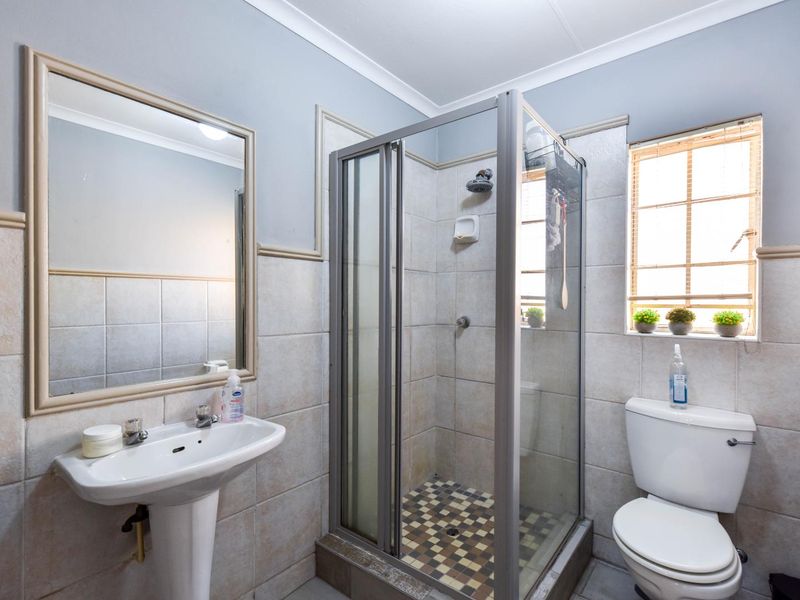 A functional bathroom featuring a pedestal washbasin, a glass-enclosed shower, and a standard toilet with neutral wall tiling.