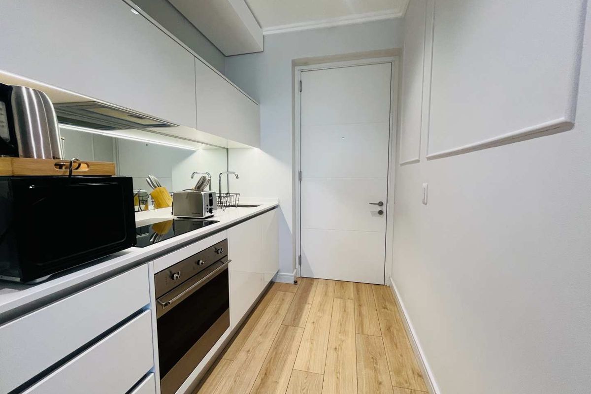 Modern galley-style kitchen featuring sleek white cabinetry, integrated oven, induction cooktop, and wood-look flooring.