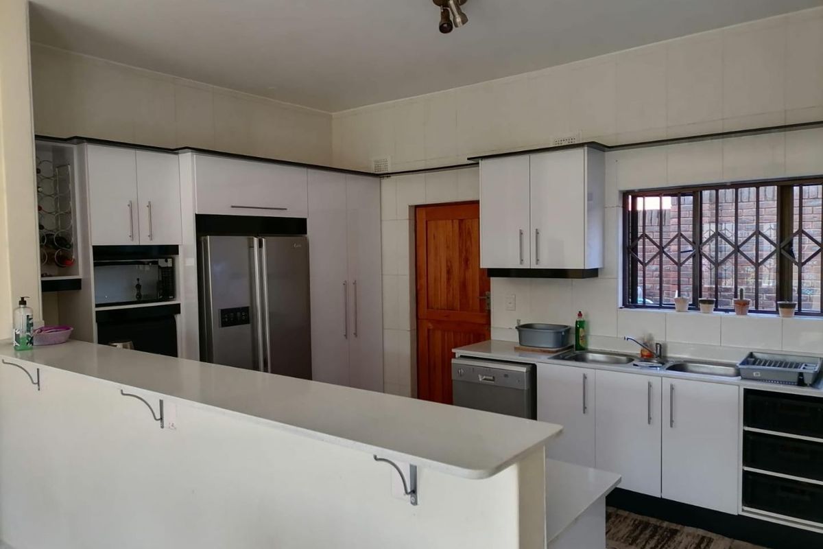 A functional kitchen featuring white cabinetry, a breakfast bar, tiled backsplash, and a window with security bars.
