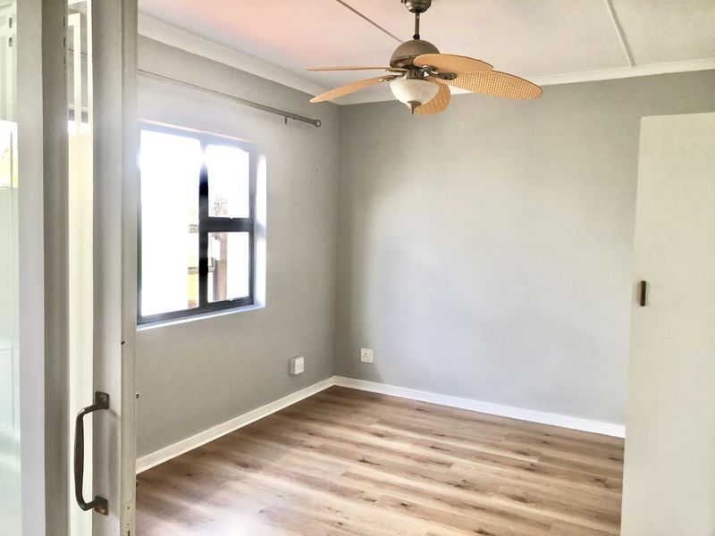 A bright, empty bedroom featuring modern laminate flooring, a ceiling fan, and a built-in cupboard, offering a clean and neutral space.