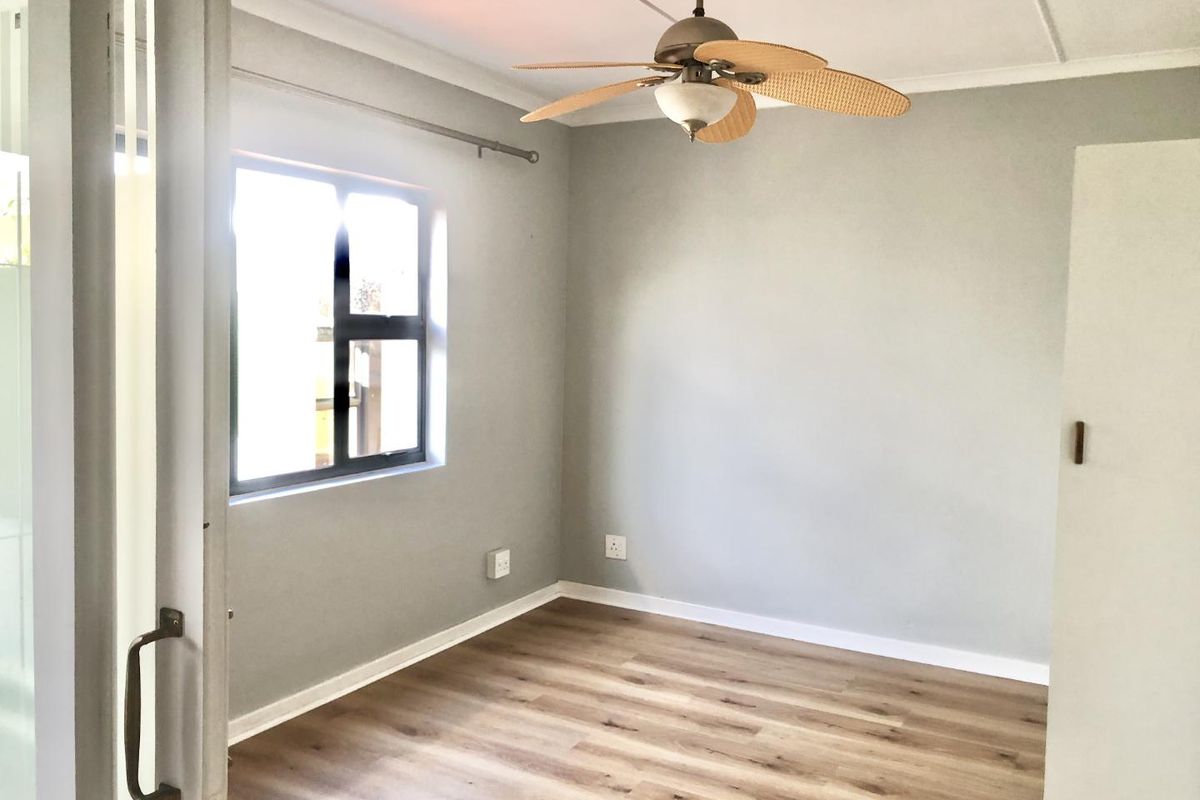 A bright, empty bedroom featuring modern laminate flooring, a ceiling fan, and a built-in cupboard, offering a clean and neutral space.