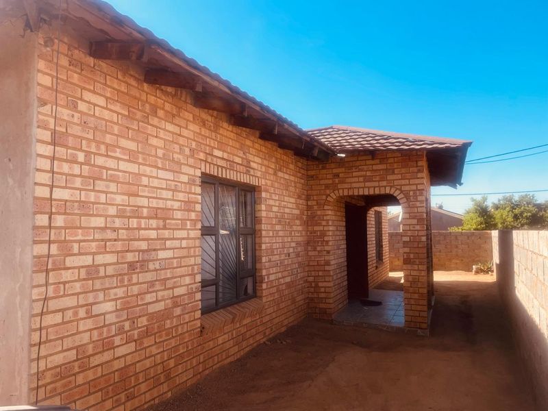A view of the rear exterior of a face brick house featuring a covered entrance, tiled roof, and perimeter walling.