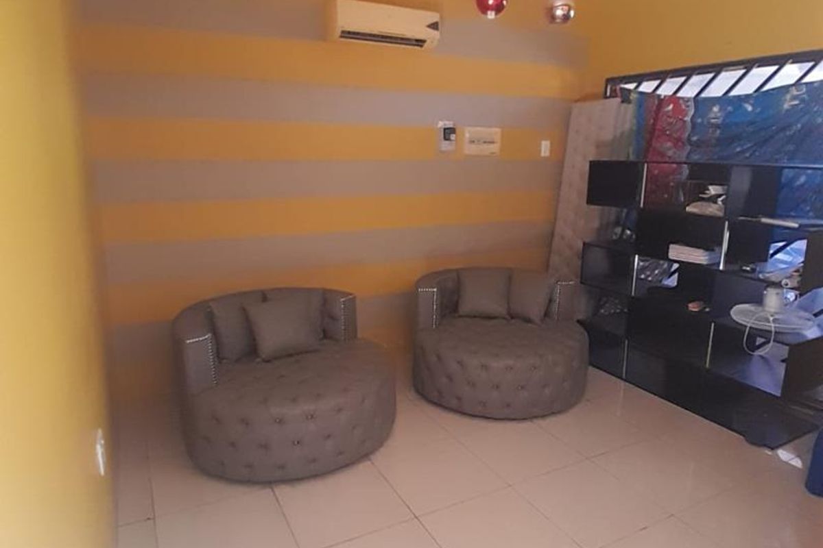 A living room featuring tiled flooring, a wall-mounted air conditioning unit, and decorative ceiling lighting, currently requiring cosmetic updates to the wall finishes.