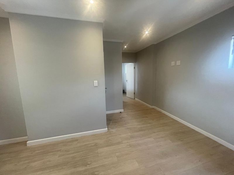 A bright, empty living area featuring modern laminate flooring, neutral grey walls, and recessed downlighting, providing a clean and versatile space.