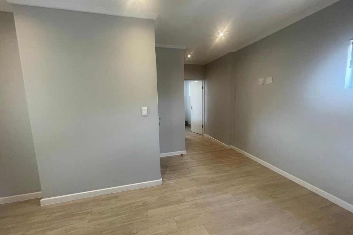 A bright, empty living area featuring modern laminate flooring, neutral grey walls, and recessed downlighting, providing a clean and versatile space.
