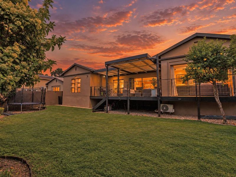 Rear view of the property featuring a raised timber deck with a pergola, overlooking a well-maintained garden at sunset.