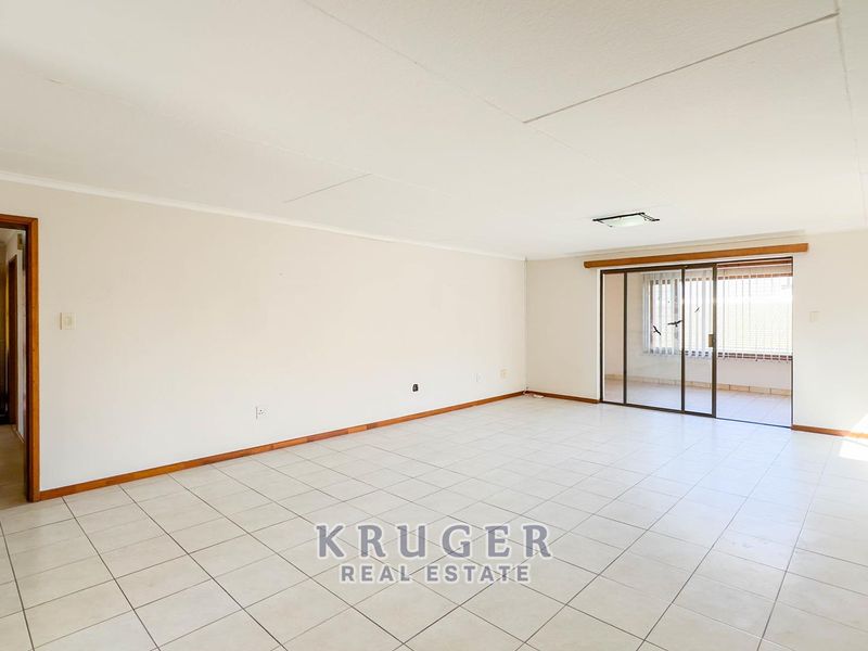 Spacious, empty living area featuring neutral tiled flooring and a sliding glass door providing access to the patio.