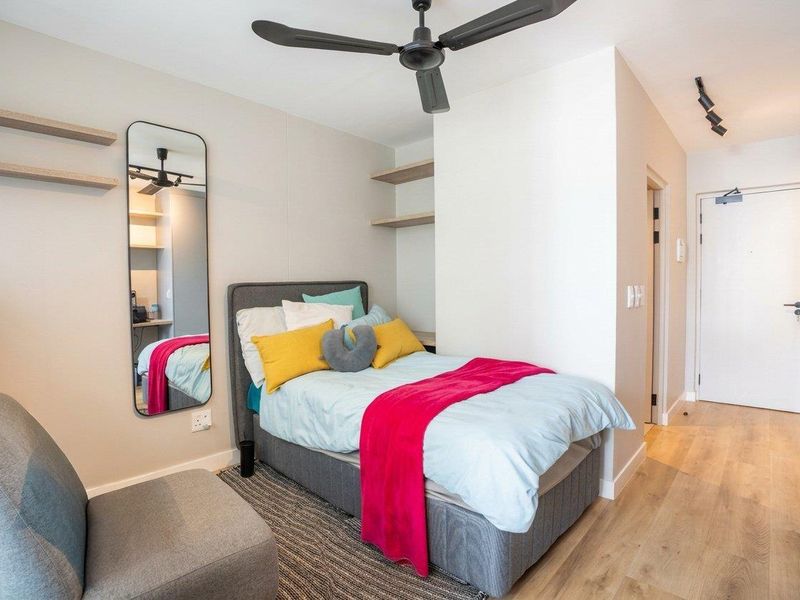 A modern, well-maintained bedroom featuring laminate flooring, built-in floating shelves, a ceiling fan, and track lighting, offering a clean and functional living space.